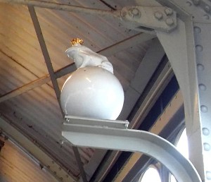 Froschkönig-Porzellanfigur auf Stahlträger unter dem Dach des U-Bahnhofs