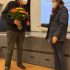 Gert Behrens und Marie Godemann stehen sich gegenüber vor einer Bühne, er hält einen Blumenstrauß in der Hand.