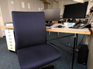 Leerer Stuhl am Schreibtisch mit zwei Bildschirmen und Telefon