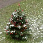 Geschmückter Weihnachtsbaum auf einer Wiese, beides mit etwas Schnee bedeckt